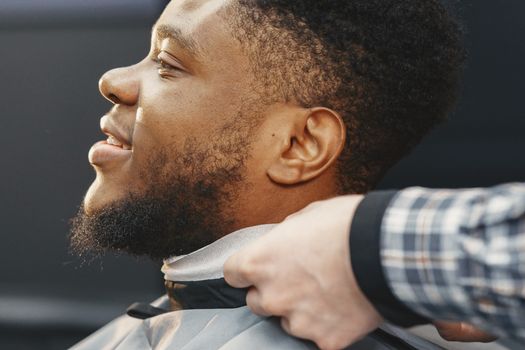 A man with a beard smiling while getting a haircut at a barbershop.