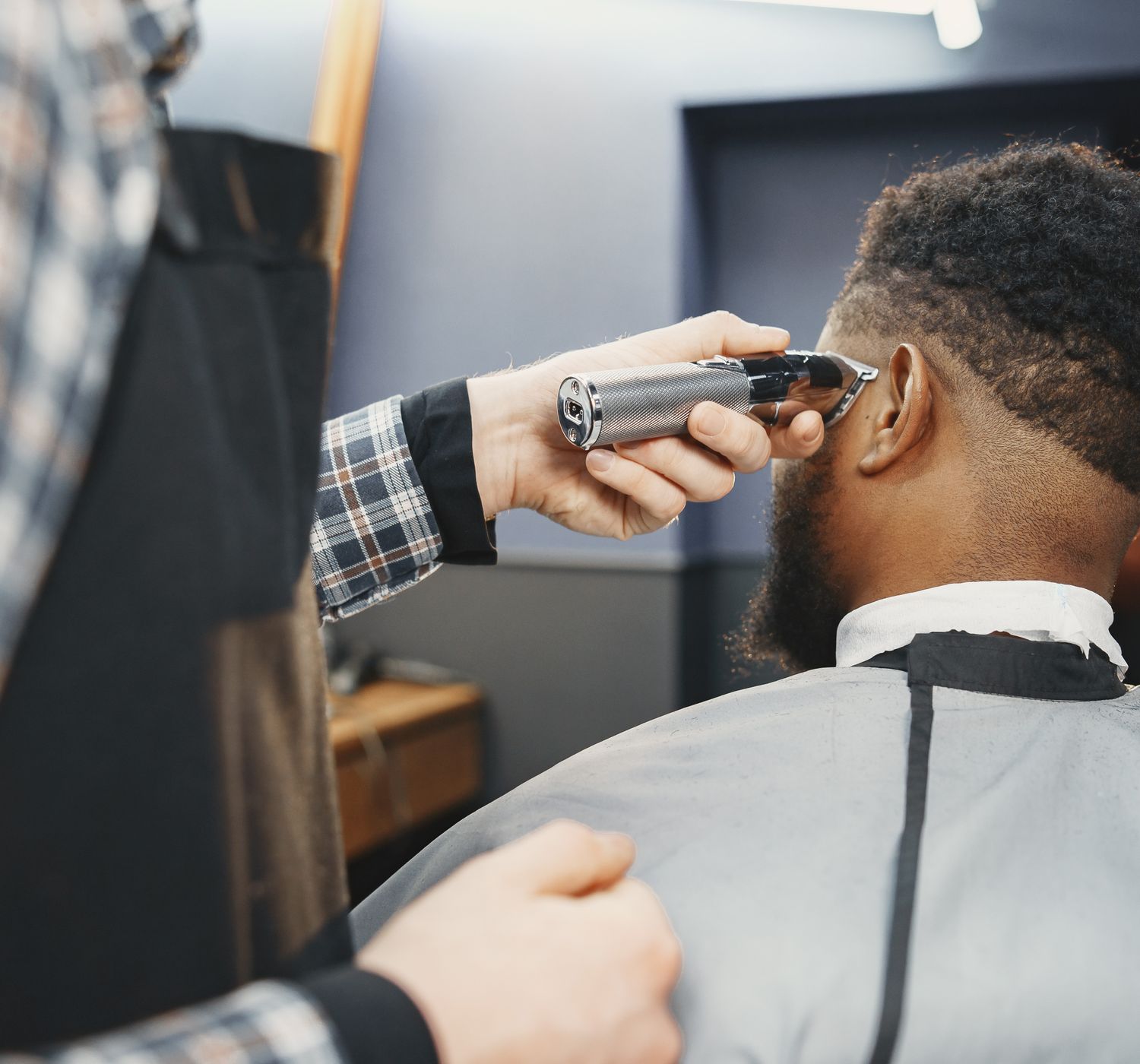 A barber uses clippers to style an African American man's hair in a salon setting.
