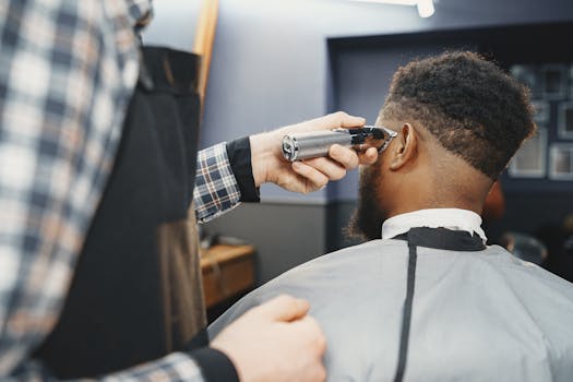 A barber uses clippers to style an African American man's hair in a salon setting.