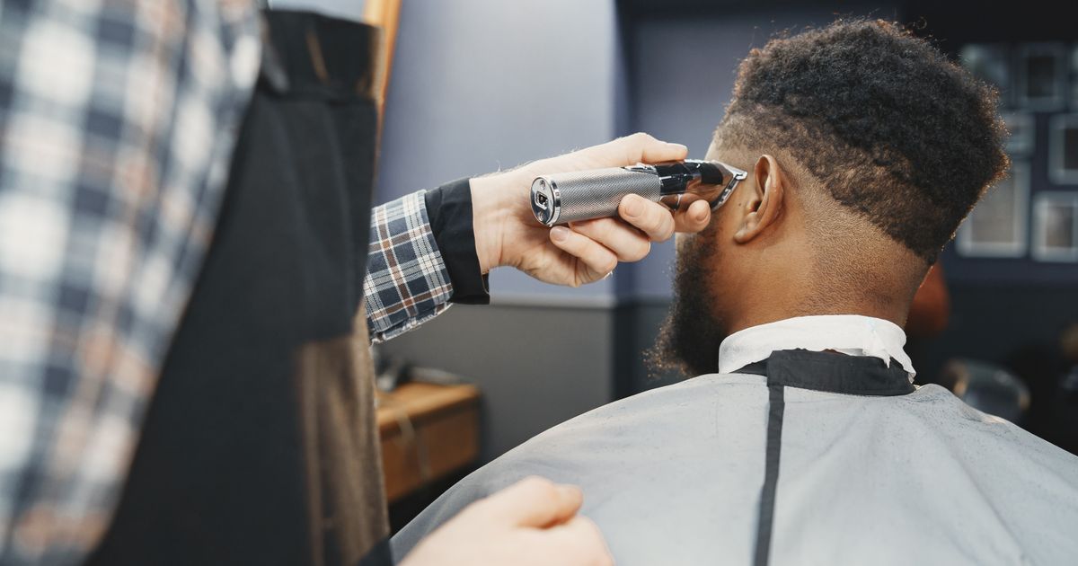 A barber tidying a man's hairline with clippers in a bright barbershop