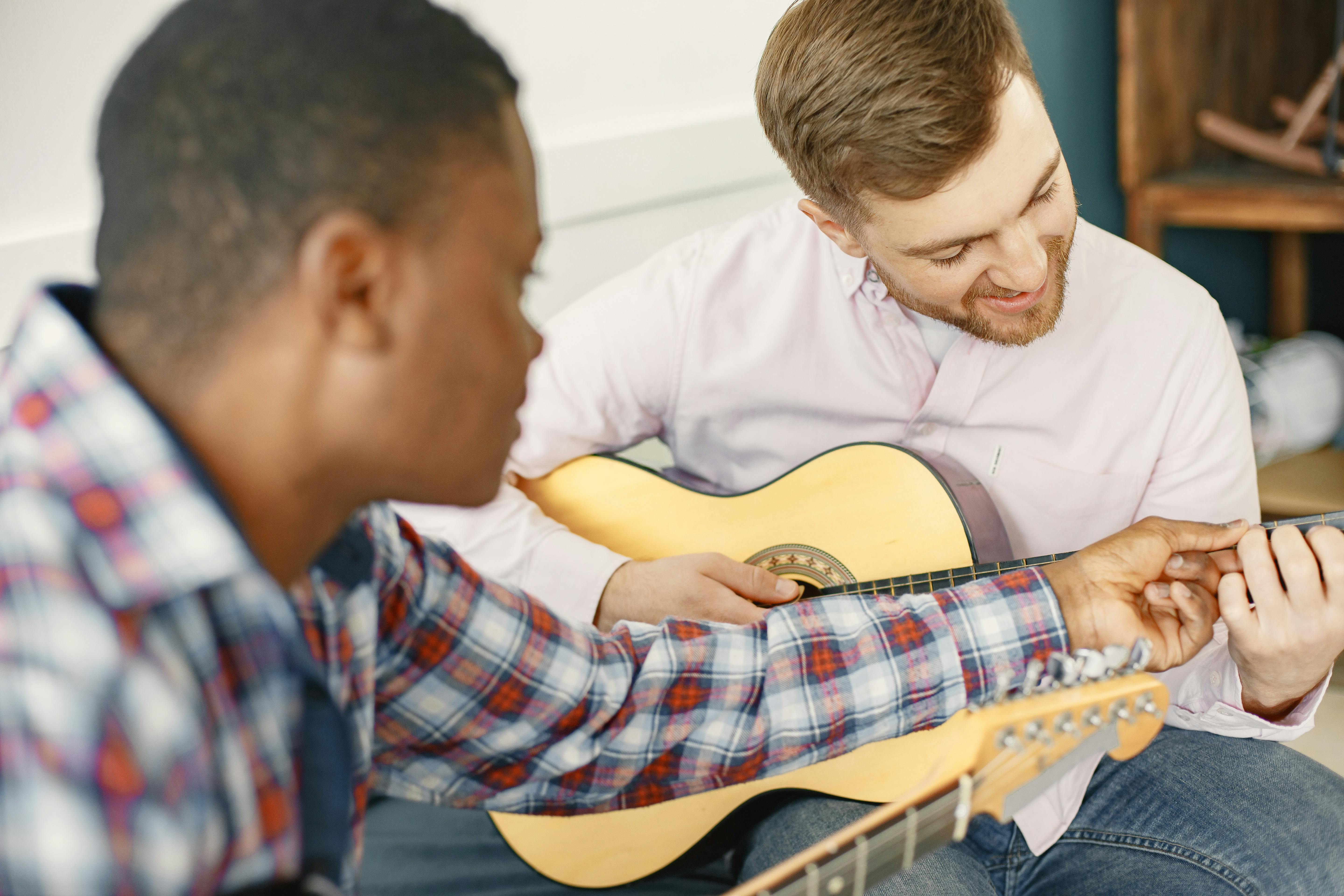 Two men enjoying a guitar lesson, one teaching and the other learning indoors.