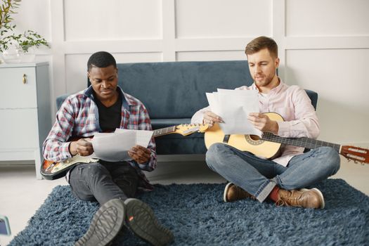 Two men sitting on rug with guitars, composing music in cozy living room.