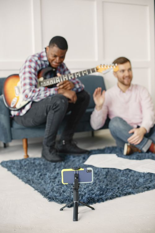 Free Two friends enjoying a music session with an electric guitar and smartphone setup. Stock Photo