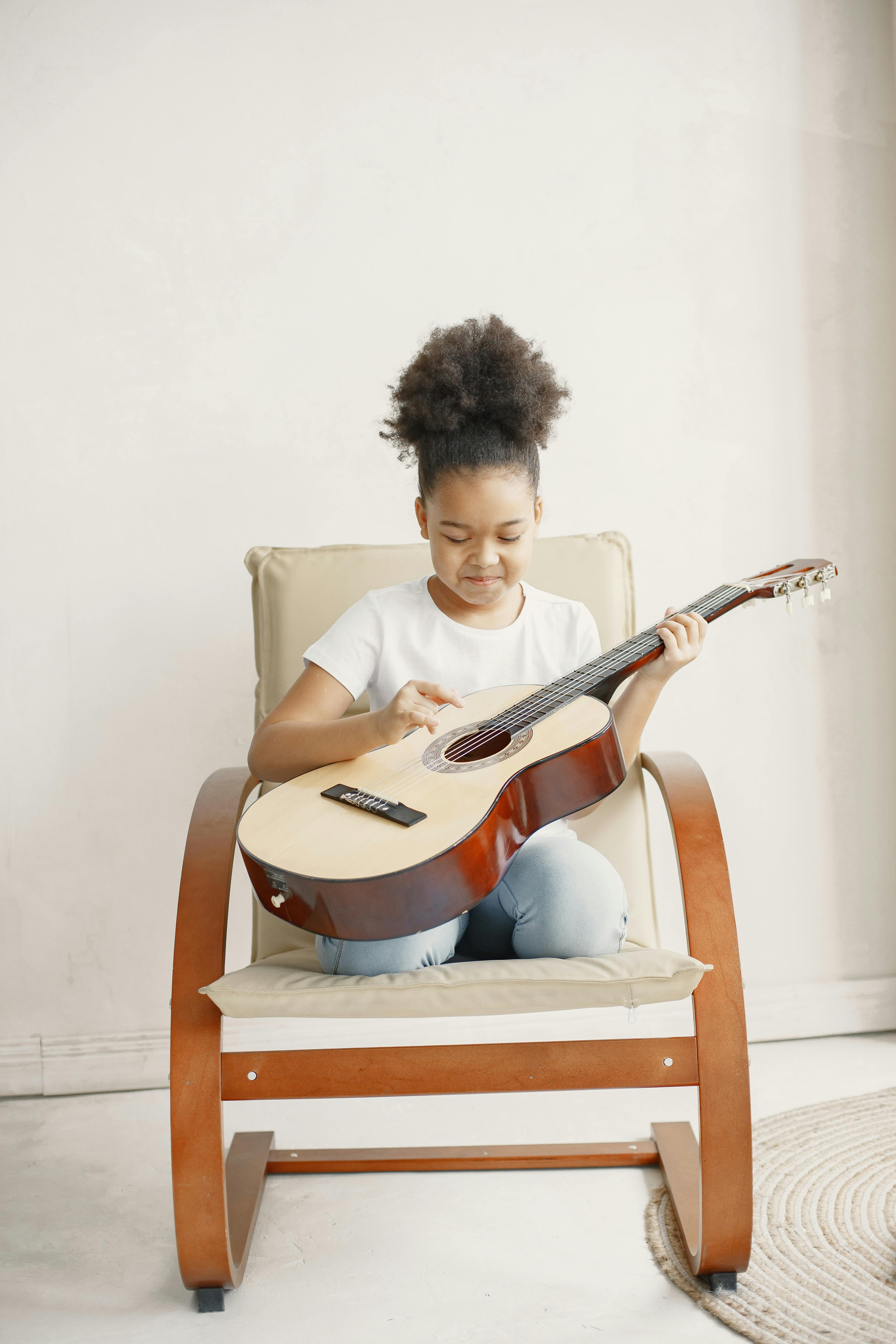 Child enjoying playing an acoustic guitar while sitting indoors on a modern chair.