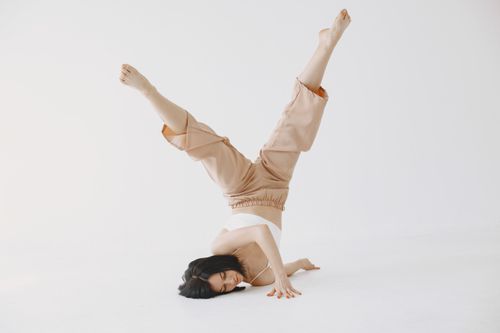 Free Young woman performs a graceful headstand pose in a minimalist studio setting. Stock Photo