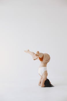 A woman in a yoga headstand pose on a light background, showcasing balance and strength.