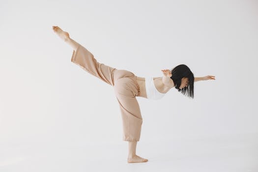 A dancer in a graceful pose with a raised leg, showcasing balance and flexibility in a minimalist setting.