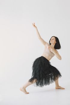 A woman gracefully posing in dance, wearing a black skirt in a well-lit studio.