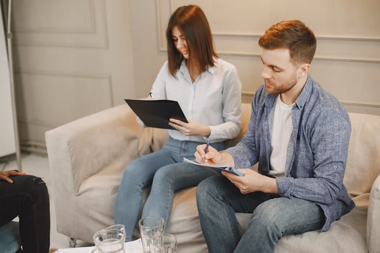 Couple Sitting On Beige Couch Signing A Contract