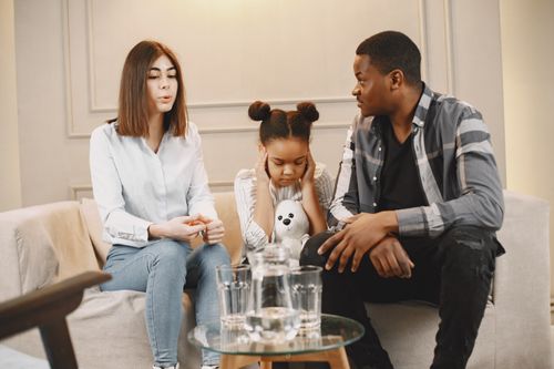 Free Parents talking to daughter covering ears on sofa. Stock Photo