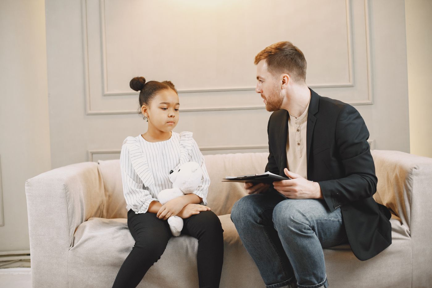 Adult support worker sitting with a young girl in a calm indoor support setting