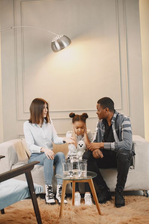 Free A family engaging in a thoughtful conversation while sitting on a stylish sofa in a modern living room. Stock Photo