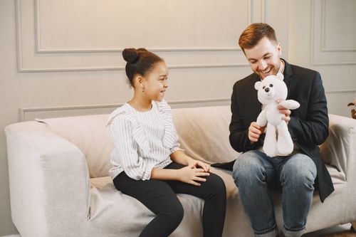 Free A joyful father and daughter sharing a happy moment with a teddy bear indoors. Stock Photo