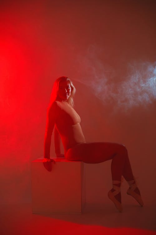 Woman Sitting On Box With Pink Smoke On Background