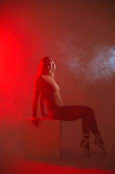 A graceful ballerina poses in red smoke lighting, exuding elegance and artistry.