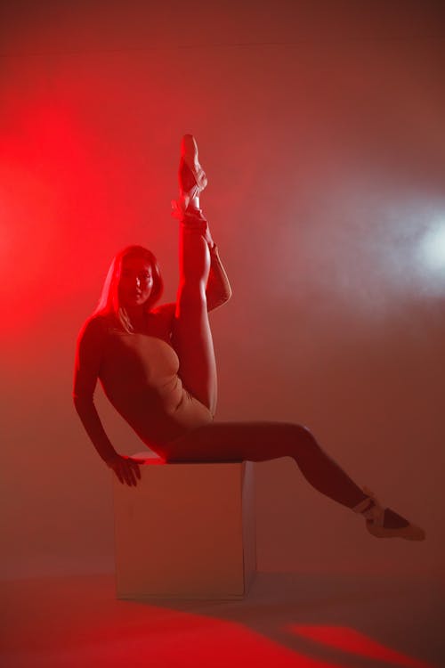 Woman Sitting on Cube Block with Leg Raised in Air
