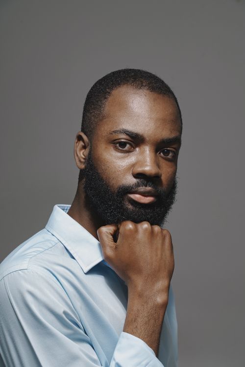 Free Portrait of an elegant man in a blue shirt with a thoughtful pose, set against a neutral background. Stock Photo