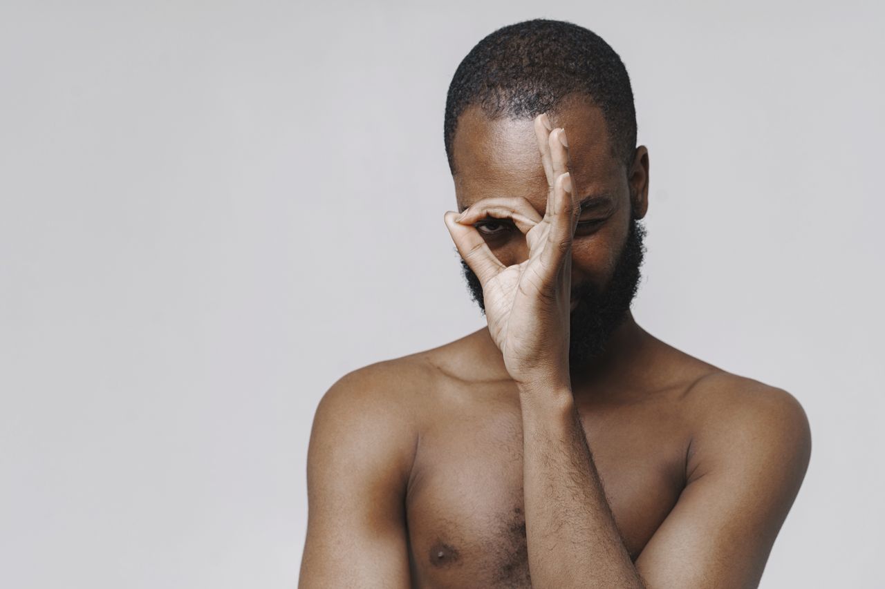 studio portrait of a playful shirtless man making an ok sign over one
