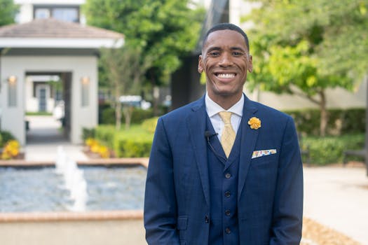 Confident man smiling in a blue suit with a yellow tie and lapel flower.