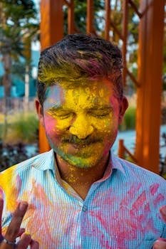 South Asian man enjoying Holi festival with vibrant colored powder on face outdoors.
