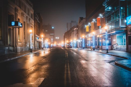 Empty asphalt road located between buildings and illuminated by streetlights in night time