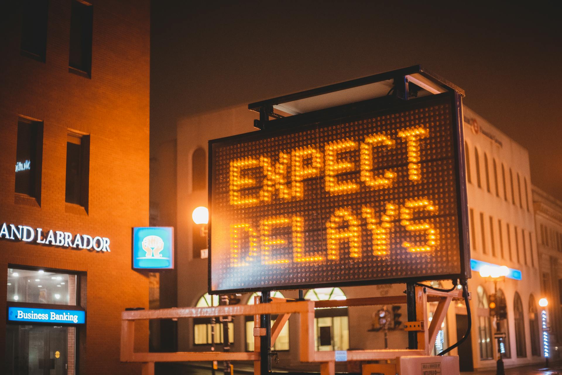 Mobile electronic traffic sign with inscription Expect delays placed on road in city street in evening time