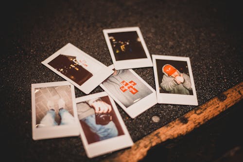 From above of instant photos placed on gray asphalt ground in evening time