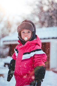 雪花飘落的户外，一个年轻的孩子穿着粉红色的冬装