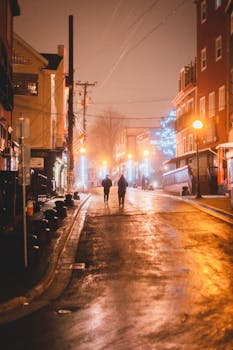 Unrecognizable people walking on wet asphalt road between residential buildings in city in evening time