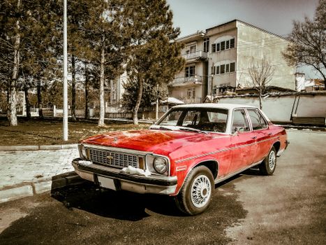A classic red Chevrolet car parked on a street lined with trees and buildings in Türkiye.