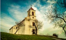 一座老教堂顶着红色屋顶，矗立在树木之间，映衬着充满活力的天空