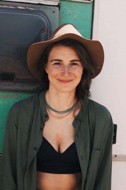 Positive young woman in trendy outfit and hat looking at camera while leaning on wall with window in daylight