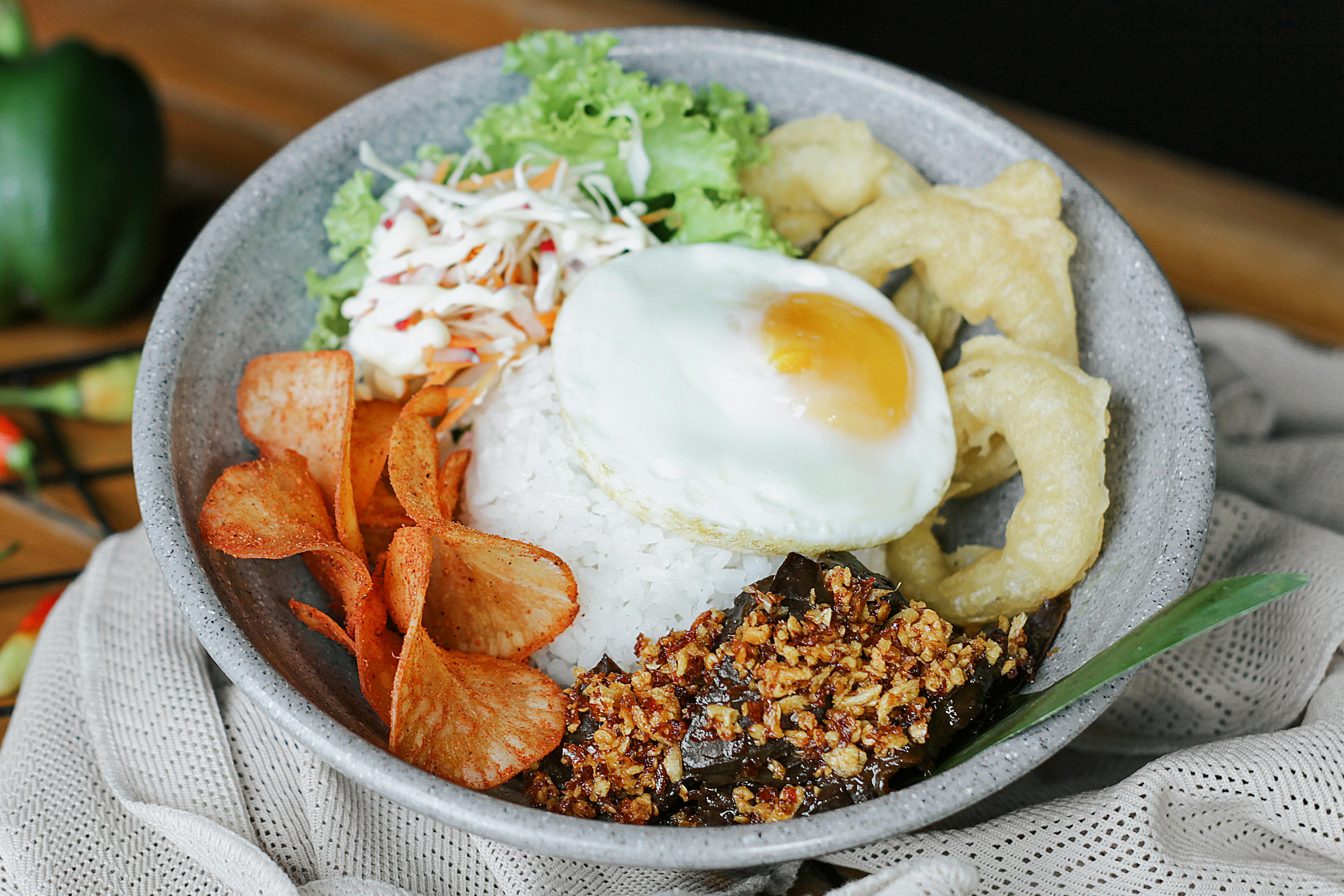 A tempting bowl of Indonesian rice topped with egg, chips, and crispy toppings.