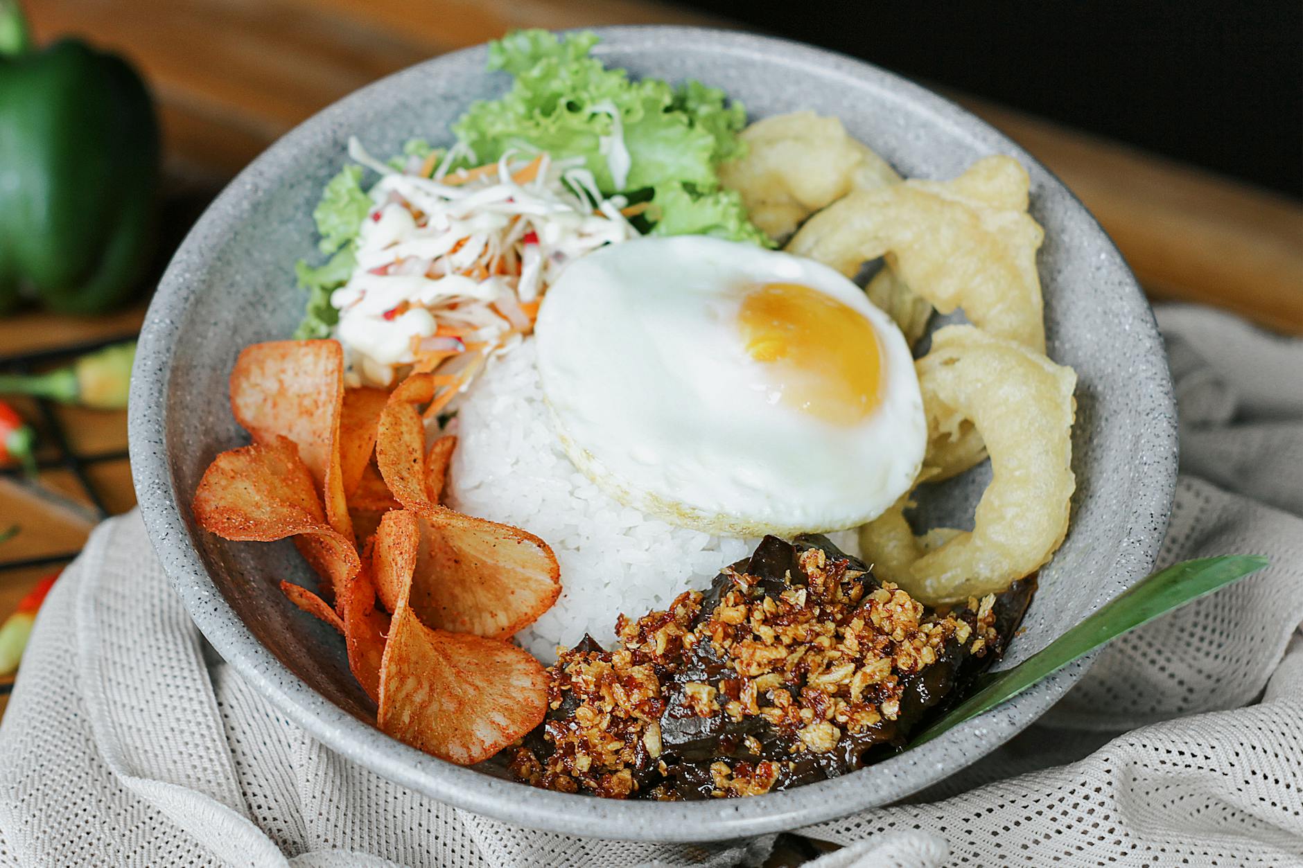 A tempting bowl of Indonesian rice topped with egg, chips, and crispy toppings.
