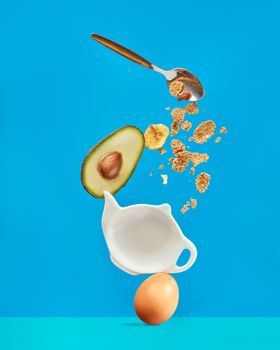 Creative composition of avocado, egg, and granola against a bright blue backdrop.