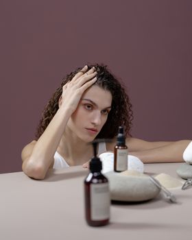 Woman with curly hair posing with skincare products and stones.