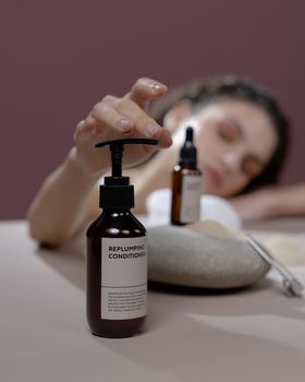 Woman's hand reaching for a replumping conditioner bottle in a serene beauty setting.