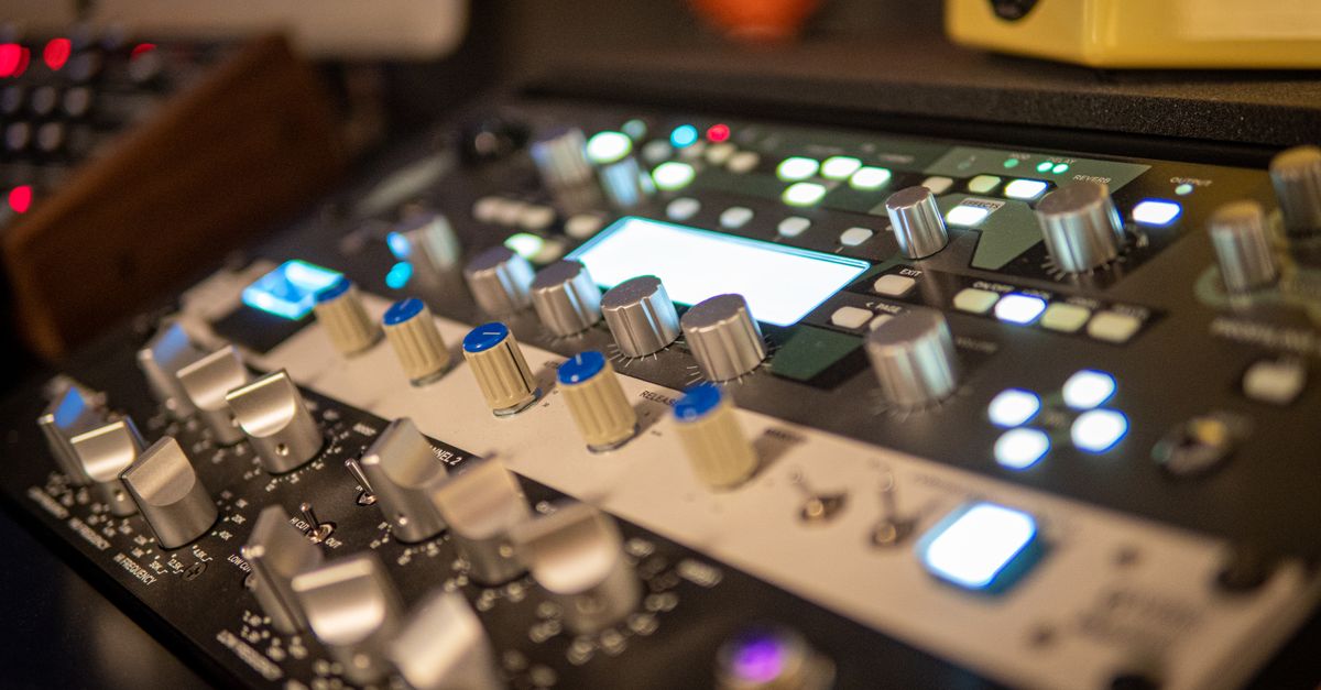 Close-up of a professional audio mixer with knobs and lights in a modern recording studio setting.