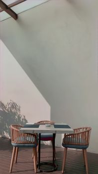 A minimalist outdoor setup with chairs and a table casting long shadows on a white wall.
