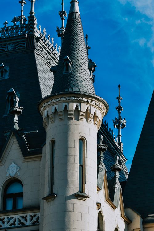Free Close-up of an ornate castle tower with gothic architecture under a blue sky. Stock Photo