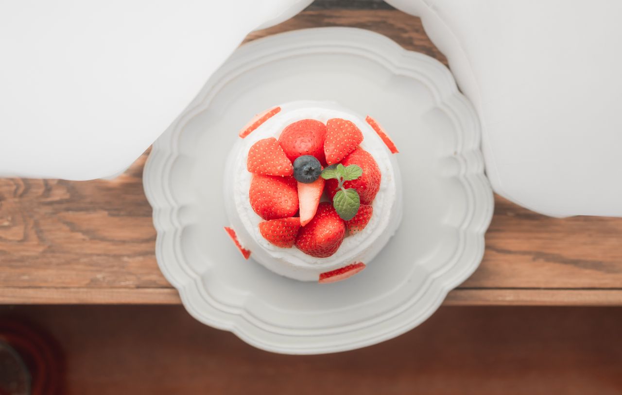 Gâteau à la crème blanche généreusement décoré de fraises rouges fraîches et d’une feuille de menthe