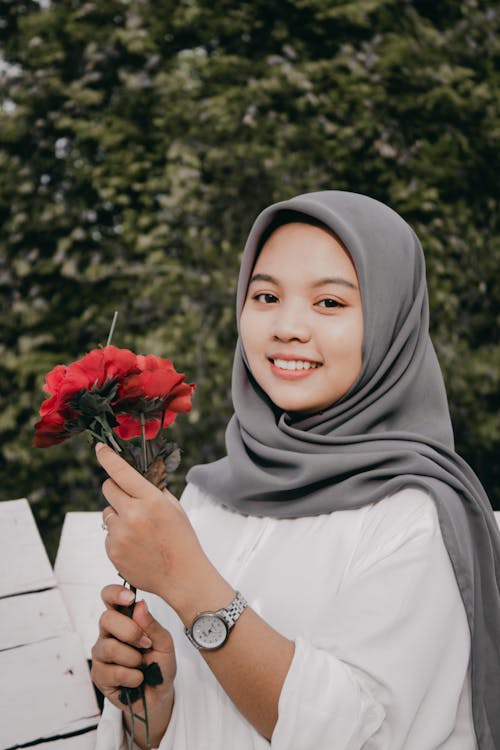 A Woman in White Long Sleeves and Headscarf Smiling while Holding Flowers
