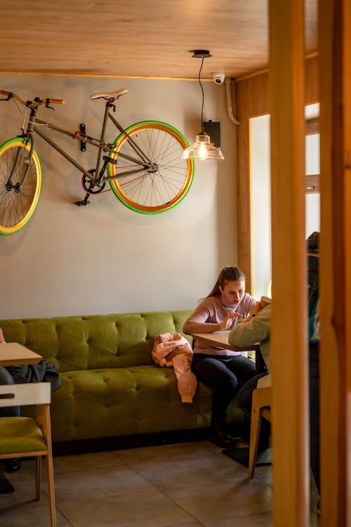 Female friends sitting on at table near window under glowing lamp against bicycle hanging on wall