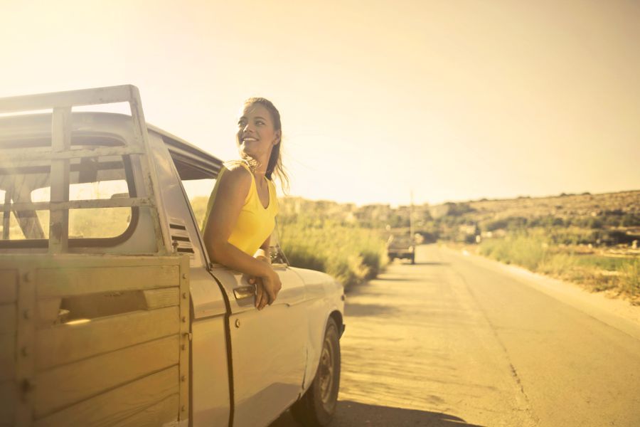 Woman leaning out of a pickup truck on a sunlit road, photo by Andrea Piacquadio on Pexels