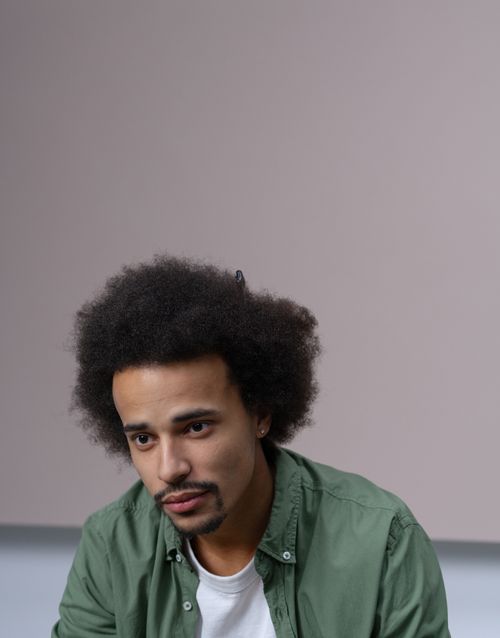 Free Studio portrait of a young African American man with afro hair in a green shirt looking thoughtful. Stock Photo