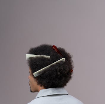 Studio portrait of a man with afro hairdo, styled with multiple combs. Minimalist background enhances focus.