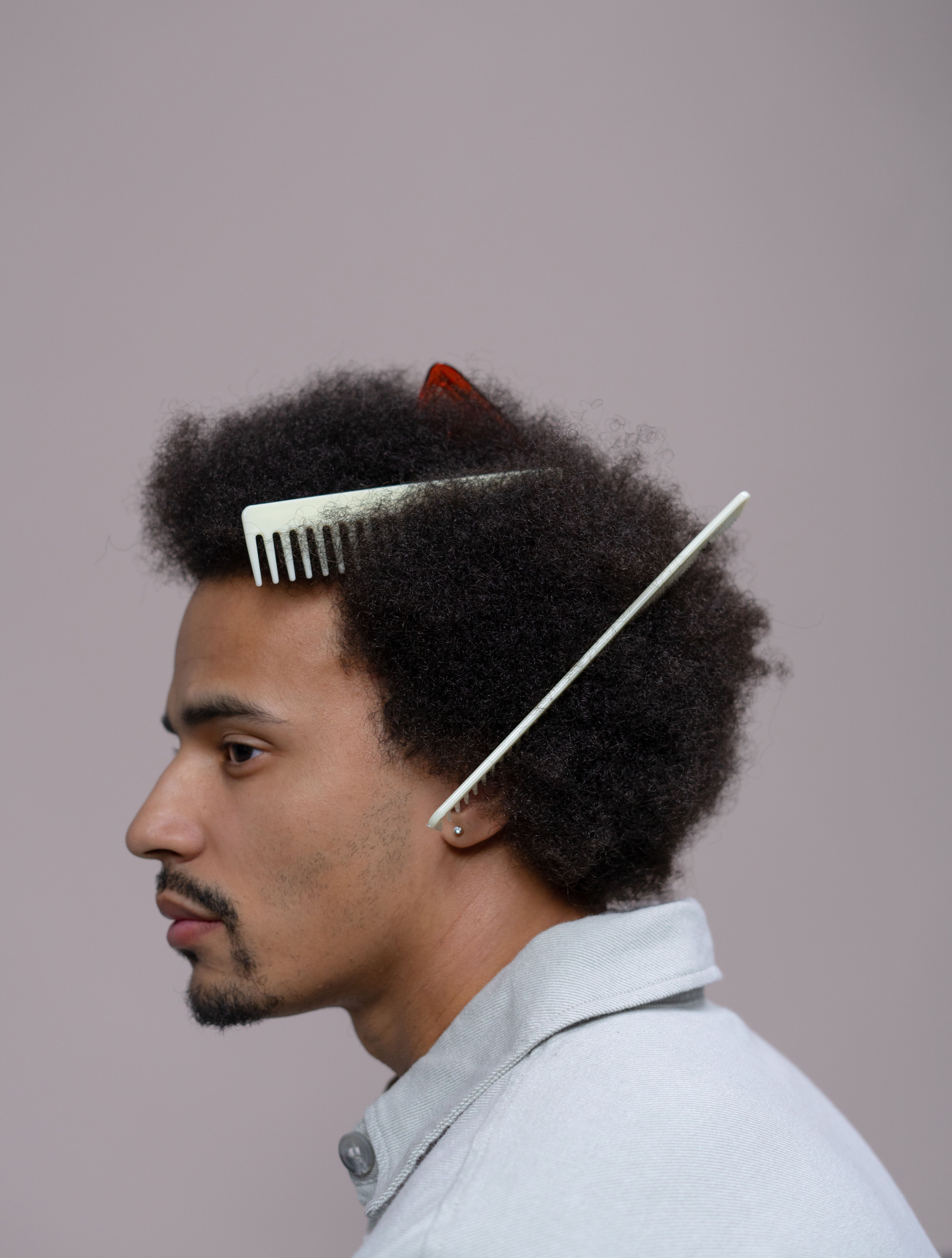 Side profile of a man with an afro hairstyle featuring two combs, one plastic and one metal.