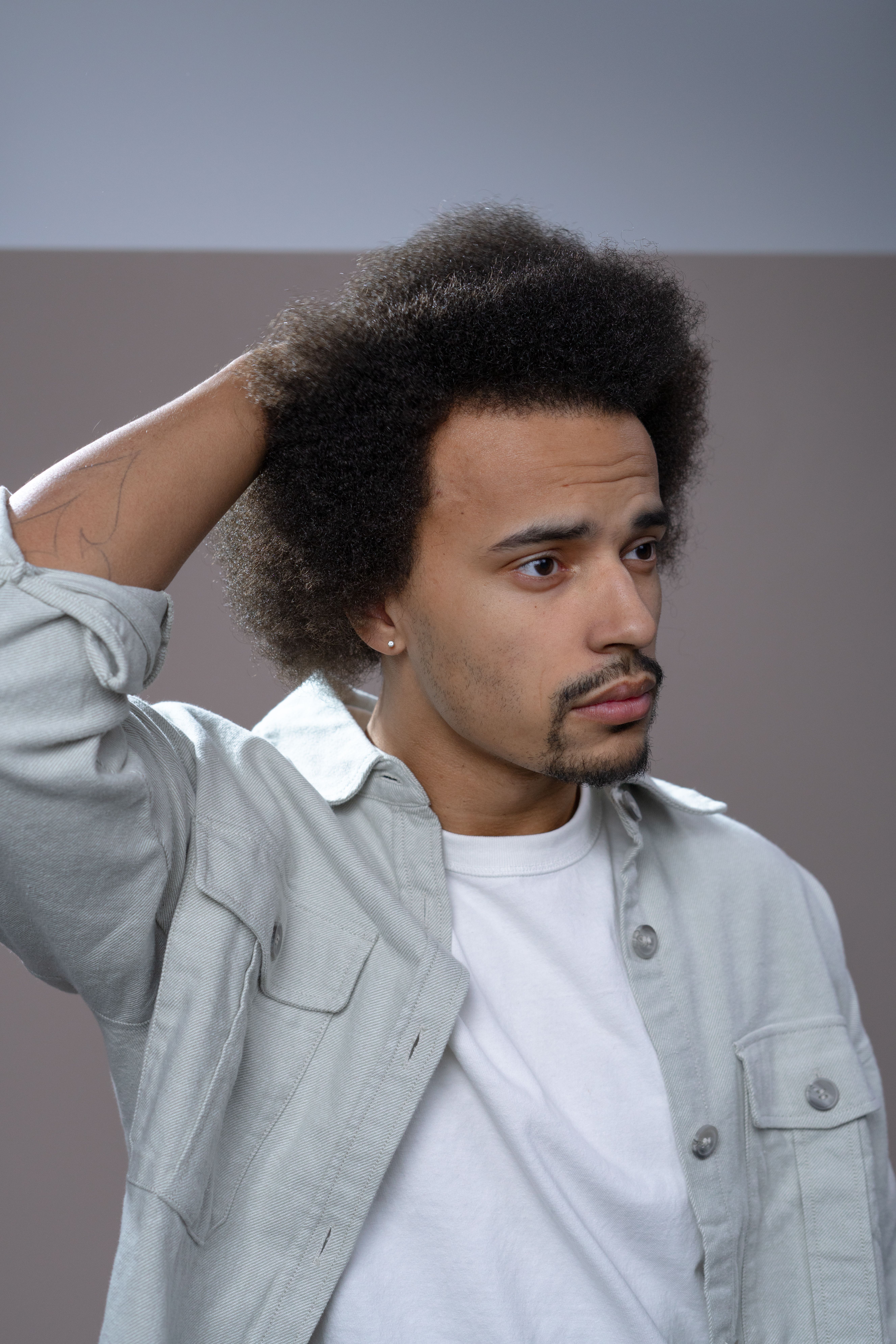A contemplative man with afro hair poses indoors, wearing a light jacket.