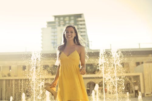 女人穿着黄色意大利面条皮带礼服站在喷泉附近