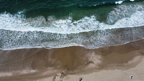 Free Drone view of ocean waves crashing on a sandy beach creating a beautiful seascape. Stock Photo